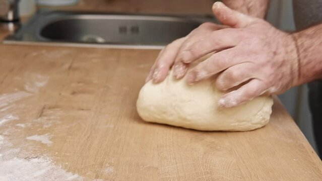 Male hands kneading dough, baking preparation closeup. Pastry Man kneads making yeast dough for pizza, burger, buns, muffins or pie. Anonymous baker. Bakery chef cooking bake in a kitchen professional