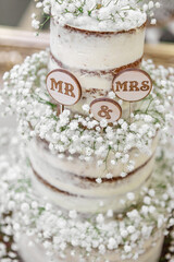 Sweet wedding cake in three tiers, decorated with small white flowers, signs and the inscription...