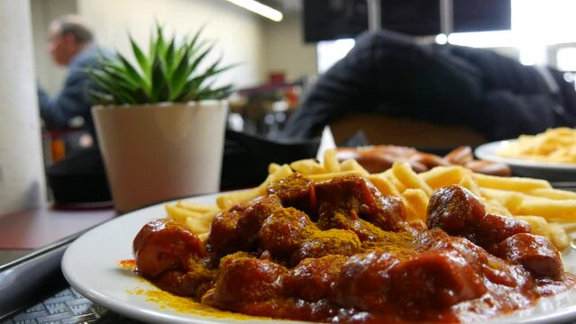 A large dish of curry sausages in tomato sauce and French fries in a restaurant. Unhealthy fatty food concept