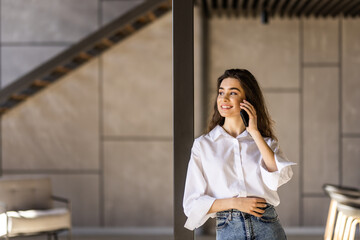 Fototapeta premium Happy woman freelancer in casual clothes talking phone with friends standing on home