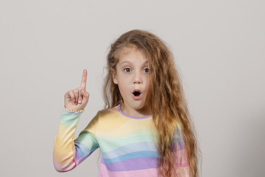 Portrait of a child girl with finger pointed up. A small child has an idea on a white board. Success, bright idea, creative ideas and innovative technology concept.