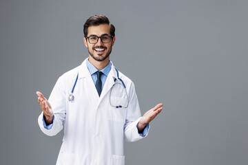 Male smile doctor in a white coat and eyeglasses and a stethoscope looks at the camera on a white...