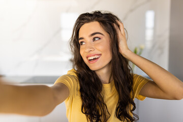 Cheerful young woman taking a selfie at the kitchen