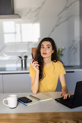 Freelancer is planning future and dreaming. Spahish woman is sitting in front of computer at home. Employee is working on project and thinking on ideas.