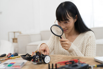 Young Asian female learning toy robotics technology through magnifying glass. Young woman building...