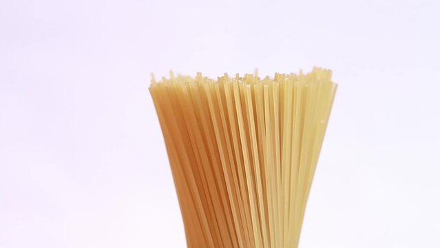 A pack of uncooked spaghetti rotates around on a light background. Side view, closeup of spaghetti pasta with copy space on the left