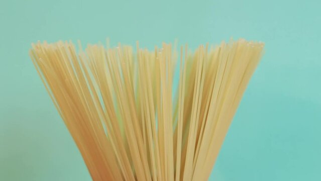 A pack of uncooked spaghetti rotates around on a blue background. Side view, closeup of spaghetti pasta