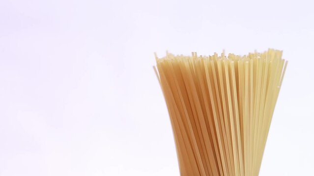 A pack of uncooked spaghetti rotates around on a light background. Side view, closeup of spaghetti pasta with copy space on the left