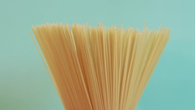 A pack of uncooked spaghetti rotates around on a blue background. Side view, closeup of spaghetti pasta