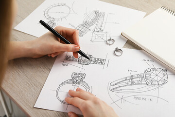 Jeweler drawing sketch of elegant ring on paper at wooden table, closeup - obrazy, fototapety, plakaty
