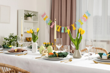 Festive Easter table setting with painted eggs, burning candles and yellow tulips in room