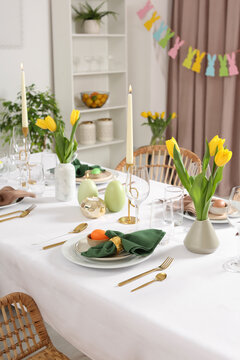Festive Easter table setting with painted eggs, burning candles and yellow tulips in room