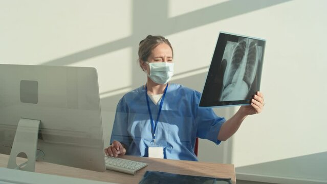 Medium portrait of female radiologist sitting at desk in her office working with X-ray pictures