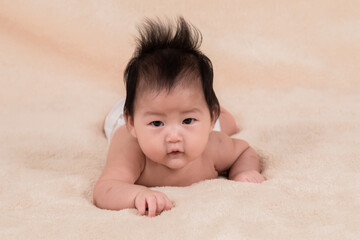 Portrait asian newborn baby 3 month lying prone on beige soft bed. healthy adorable infant without clothes looking for mom want to play with mother while she work, baby feel hungry want milk.