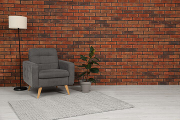 Cosy armchair, lamp and potted plant near brick wall in room, space for text. Interior design