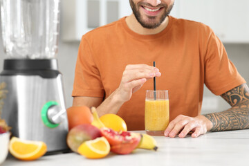 Man with delicious smoothie at white marble table in kitchen, closeup