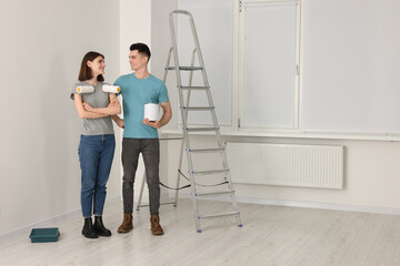 Young couple with painting tools near metal stepladder indoors. Room renovation