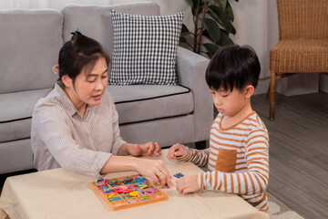 Asian happy single mother and handsome son playing alphabet games with plastic toys into the word...