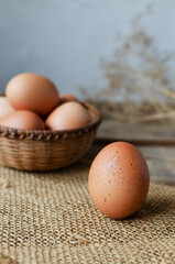 Chicken eggs in a wicker bowl on burlap on a wooden background. Rustic style. The concept of organic food. Selective focus. Vertical orientation.