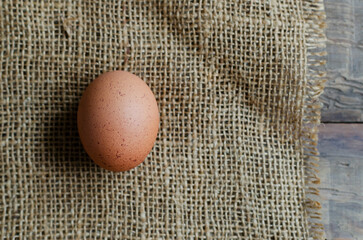 One chicken egg on burlap on wooden background. Rustic style. The concept of organic food. Top view. Copy space. Horizontal orientation.