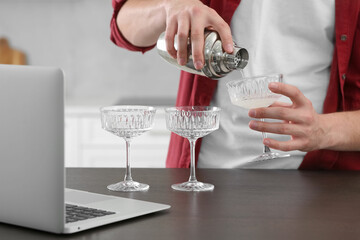 Man learning to make cocktail with online video on laptop at wooden table in kitchen, closeup. Time for hobby