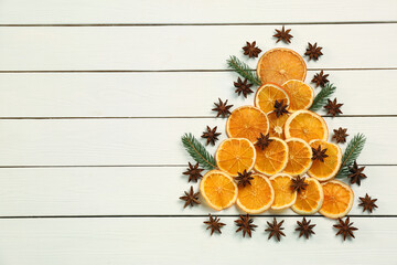 Flat lay composition with dry orange slices, fir branches and anise stars arranged in shape of Christmas tree on white wooden table. Space for text