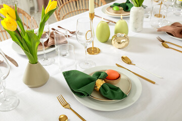 Festive Easter table setting with painted eggs, burning candles and yellow tulips - obrazy, fototapety, plakaty