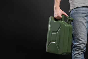 Man holding khaki metal canister on black background, closeup. Space for text
