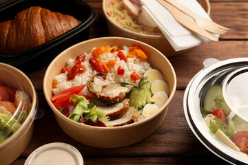 Tasty food in containers with knife and fork on wooden table