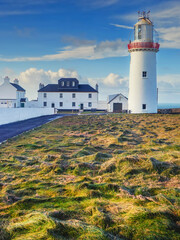 Fototapeta na wymiar Buildings and Loop head Lighthouse in county Clare, Ireland. Popular travel landmark and sightseeing area. Cloudy sky. Irish history.
