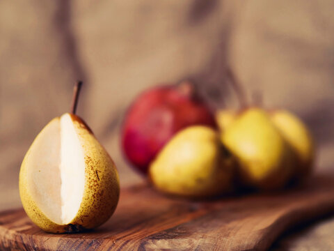 Still life with ripe pears and pomegranate on a wooden board and hessian cloth background. Selective focus. Soft and dreamy look.