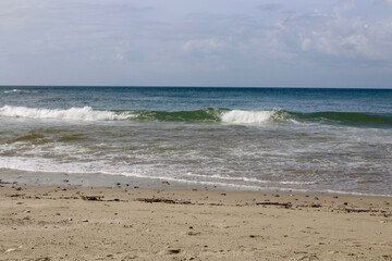 Sandy beach of a tropical island. Overcast weather. Sea wave rolls on the sandy beach.