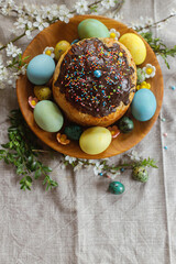 Homemade easter bread and natural dyed easter eggs with spring flowers on wooden plate on rustic table. Top view. Happy Easter! Traditional Easter food.
