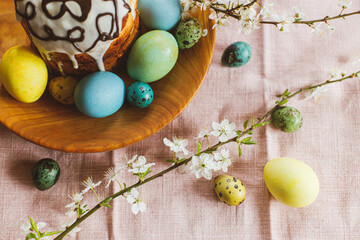 Fototapeta na wymiar Homemade easter bread and natural dyed easter eggs with spring flowers on wooden plate on rustic table. Top view. Happy Easter! Traditional Easter food.