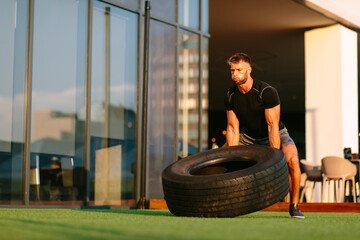Handsome young man working out in an outdoor gym and flipping tire