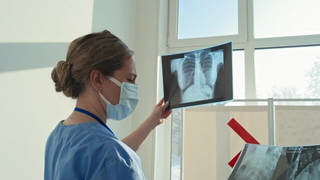 Professional radiologist wearing mask reading patients X-ray images at work in hospital