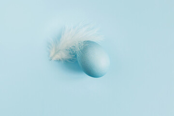 Happy Easter! Easter egg and feather on blue background flat lay. Minimal Easter still life. Modern spring banner or greeting card, space for text. Natural painted blue egg