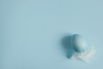 Happy Easter! Easter egg and feather on blue background flat lay. Minimal Easter still life. Modern spring banner or greeting card, space for text. Natural painted blue egg