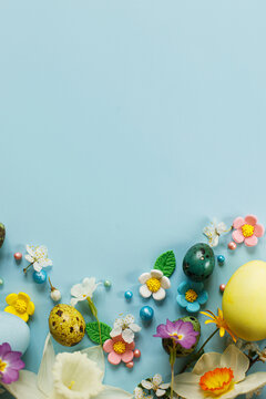 Stylish easter eggs, candy and blooming flowers on blue background flat lay. Happy Easter! Natural painted colorful eggs and spring blossom. Modern greeting card or banner, copy space