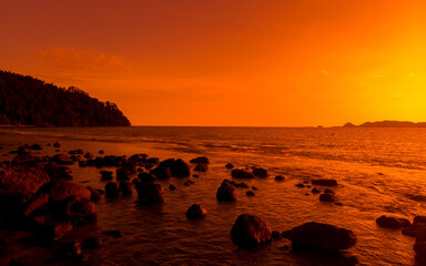 Fototapeta na wymiar Ocean orange sunset landscape with rocks in silhouette