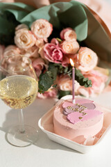cupcake with a candle and the inscription happy birthday. A cake, a glass of champagne and flowers