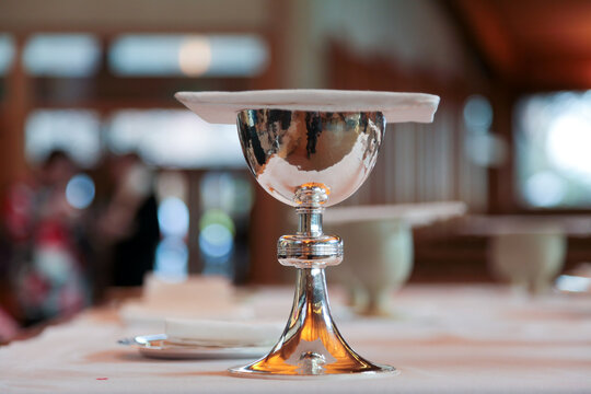 A shining silver communion chalice containing wine, a sacrament,  is covered with a chalice pall is resting on a table in an anglican church