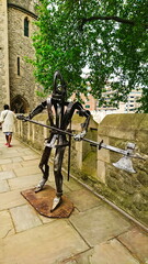 Tower of London, London, United Kingdom - May 14, 2018: iron or steel statue of a warrior attacking using an axe on the wall of a fortress under a tree crown