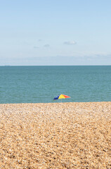 Fototapeta na wymiar Shingle beach with colorful umbrella on the horizon