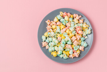 Multicolor sugary glazed popcorn on gray plate on a pink background top view