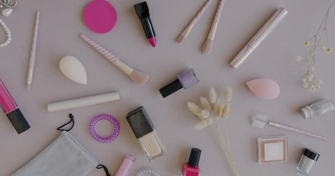 Close-up of diverse female accessories and make-up products and female hand putting flower designing flat lay against gray color background