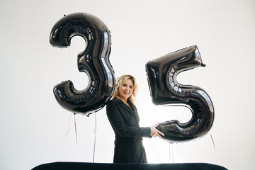 a sexy blonde in a black on background of balloons of numbers thirty-five