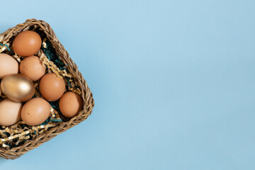 Gift basket with easter eggs, golden and natural color eggs in basket. Top view on eggs above pastel blue background.