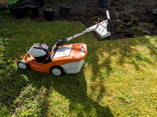 A lush green lawn, newly renovated for the upcoming summer season, is seen from above under bright sunshine. Anticipation fills the garden as a vehicle and lawn mower await their day of use.