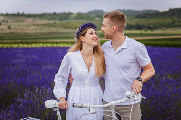 The young couple is standing in a lavender field in a smiling mood with a white bicycle